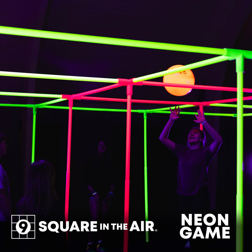 Fun game that glows under blacklight. Indoor Use. Student playing 9 Square in the Air with a glowing NEON  orange ball and pink and yellow game set.