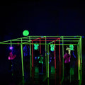 Multiple kids dressed in neon colors playing NEON 9 Square in the Air glowing under blacklight in a dark room. 